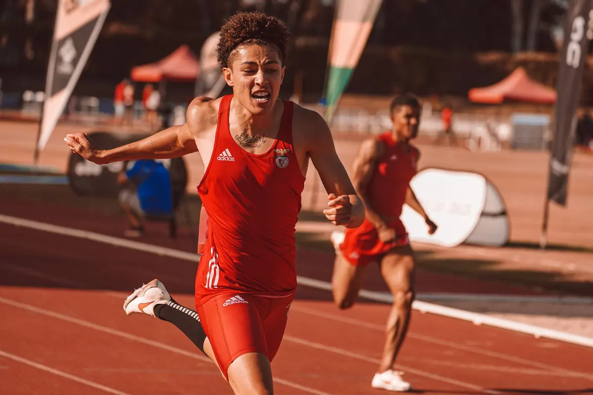 An athlete in a red kit sprinting on an athletics track