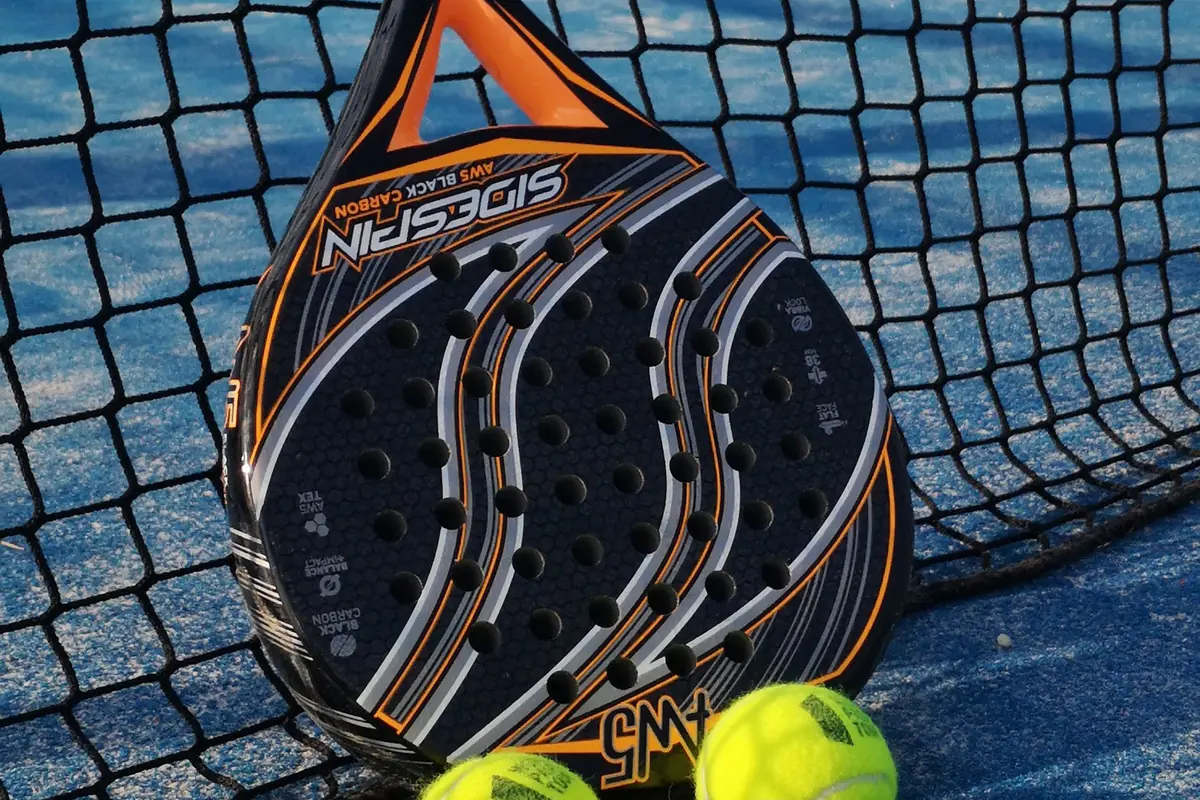 A padel racket and yellow balls in front of the net