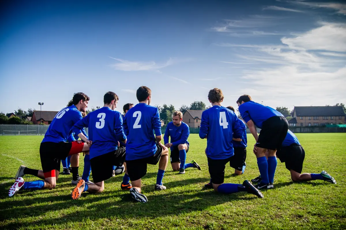 A football team in blue kits kneeling together on the pitch