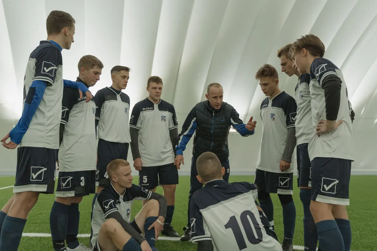 A coach gives tactics to his team gathered in a circle on an indoor pitch