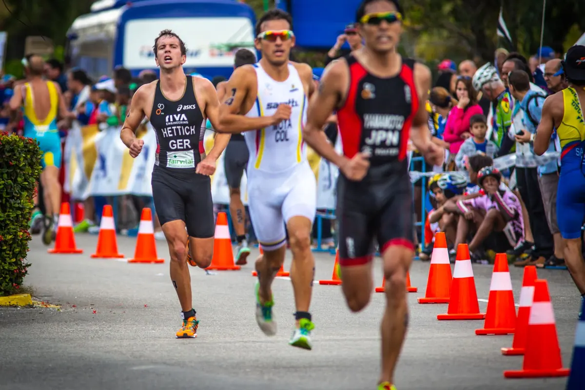 Three triathletes race side by side in front of a crowd