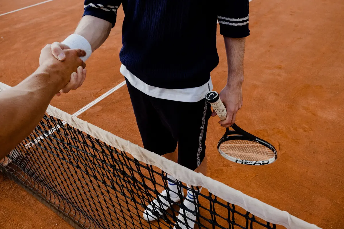 On a tennis court, two players shake hands over the net at the end of a match