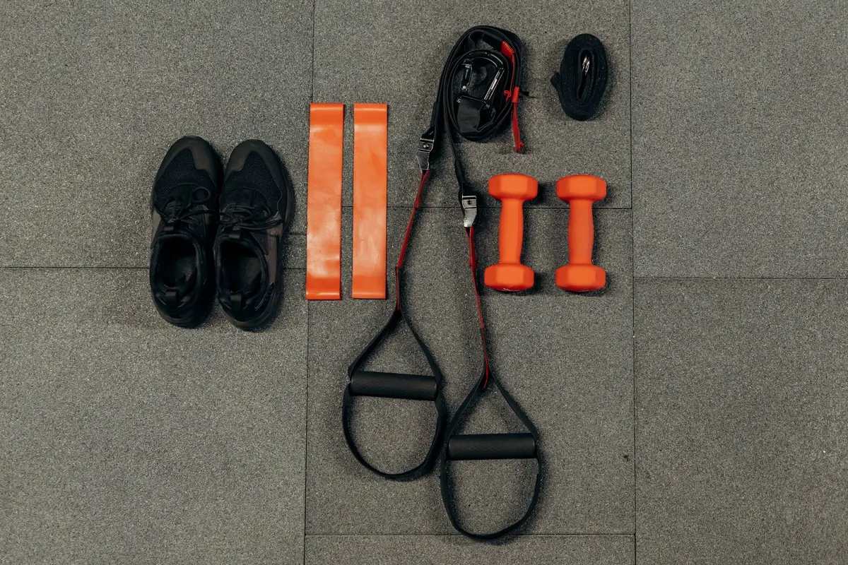 Running shoes, dumbbells and resistance bands laid out on the floor